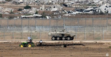  A farmer works on a field as an Israeli army vehicle moves along the separation fence on the border with the Gaza Strip in southern Israel, Sept. 19, 2025. (AFP Photo)