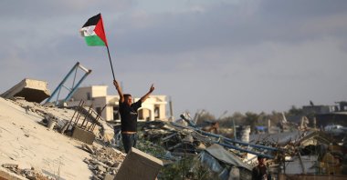 A displaced Palestinian child waves a Palestinian national flag as he stands on the rubble of a destroyed building at the Bureij camp for refugees in the central Gaza Strip, Palestine, Sept. 22, 2025. (AFP Photo)