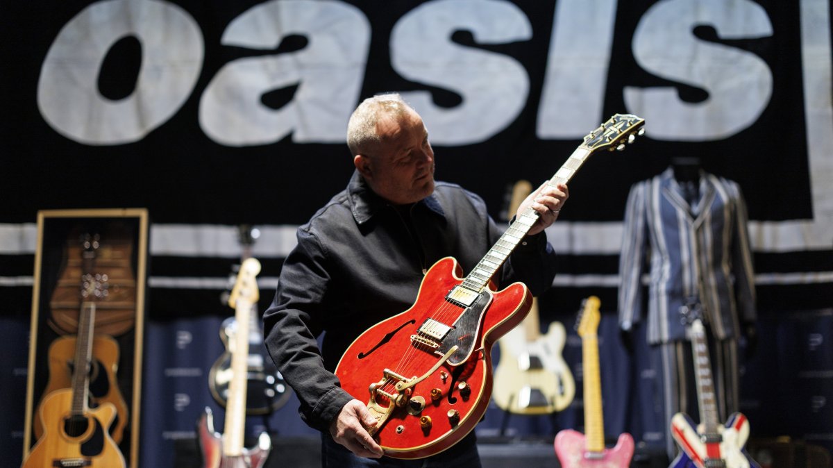 A gallery staff member poses with English singer and songwriter Noel Gallagher&#039;s 1960 Cherry Red Gibson ES-355 guitar, which was damaged by Liam Gallagher in 2009 and led to the breakup of English rock band Oasis, Hertfordshire, U.K., Sept. 24, 2025. (EPA Photo)