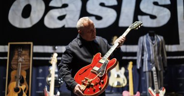 A gallery staff member poses with English singer and songwriter Noel Gallagher&#039;s 1960 Cherry Red Gibson ES-355 guitar, which was damaged by Liam Gallagher in 2009 and led to the breakup of English rock band Oasis, Hertfordshire, U.K., Sept. 24, 2025. (EPA Photo)