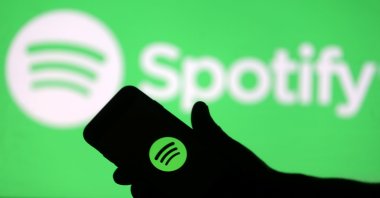 A smartphone is seen in front of a screen projection of the Spotify logo, in this picture illustration taken April 1, 2018. (Reuters File Photo)