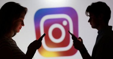Teenagers pose for a photo while holding smartphones in front of a Instagram logo in this illustration taken on Sept. 11, 2025. (Reuters Photo)