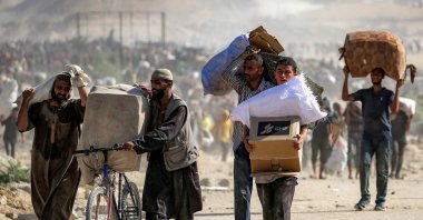 People walk with humanitarian aid packages that they received from a distribution center run by the US and Israeli-backed Gaza Humanitarian Foundation (GHF), at the so-called &quot;Netzarim corridor&quot;, Nuseirat, Gaza Strip, Palestine, Sept. 30, 2025. (AFP Photo)