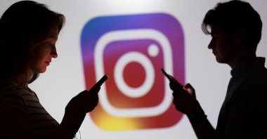Teenagers pose for a photo while holding smartphones in front of an Instagram logo in this illustration taken Sept. 11, 2025. (Reuters Photo)
