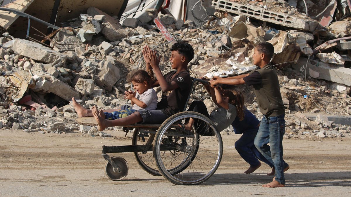 Displaced Palestinian children push two others on a wheelchair past a destroyed building at the Bureij refugee camp in the central Gaza Strip, Palestine, Oct. 6, 2025. (AFP Photo)