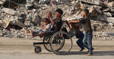 Displaced Palestinian children push two others on a wheelchair past a destroyed building at the Bureij refugee camp in the central Gaza Strip, Palestine, Oct. 6, 2025. (AFP Photo)