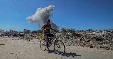 A Palestinian man rides a bicycle as an explosion from an Israeli attack is seen in the background, Gaza Strip, Palestine, Oct. 7, 2025. (AA Photo)
