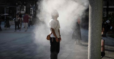 This picture shows a man resting under a water misting system to cool down on a hot day, Tokyo, Japan, Sept. 6, 2025. (AFP Photo)