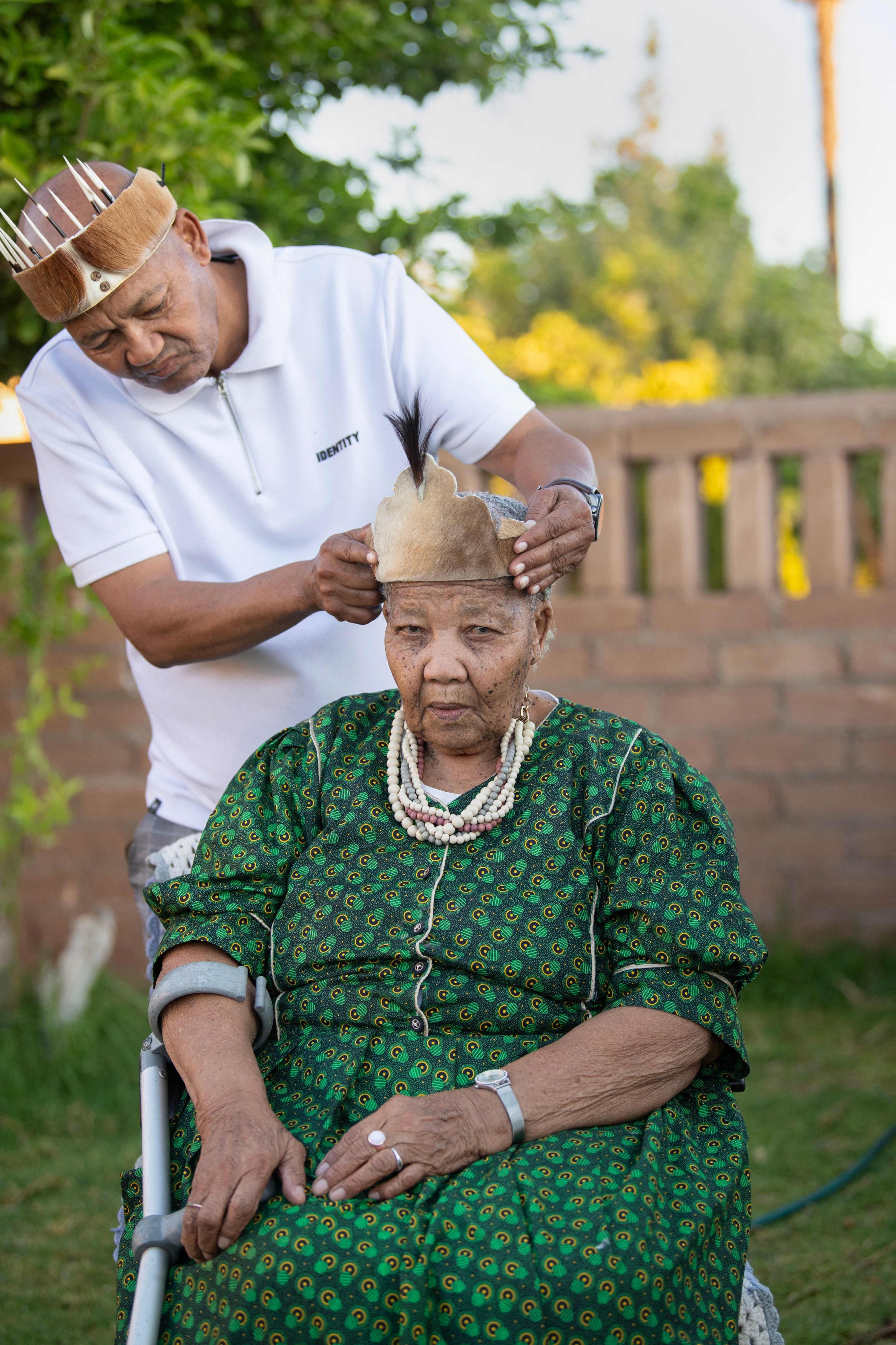 Charles Esau (L) adjusts his mother Katrina Esau's traditional headpiece, as she sits outside at her home near Upington, Northern Cape Province, South Africa, Sept. 25, 2025. (AFP Photo)