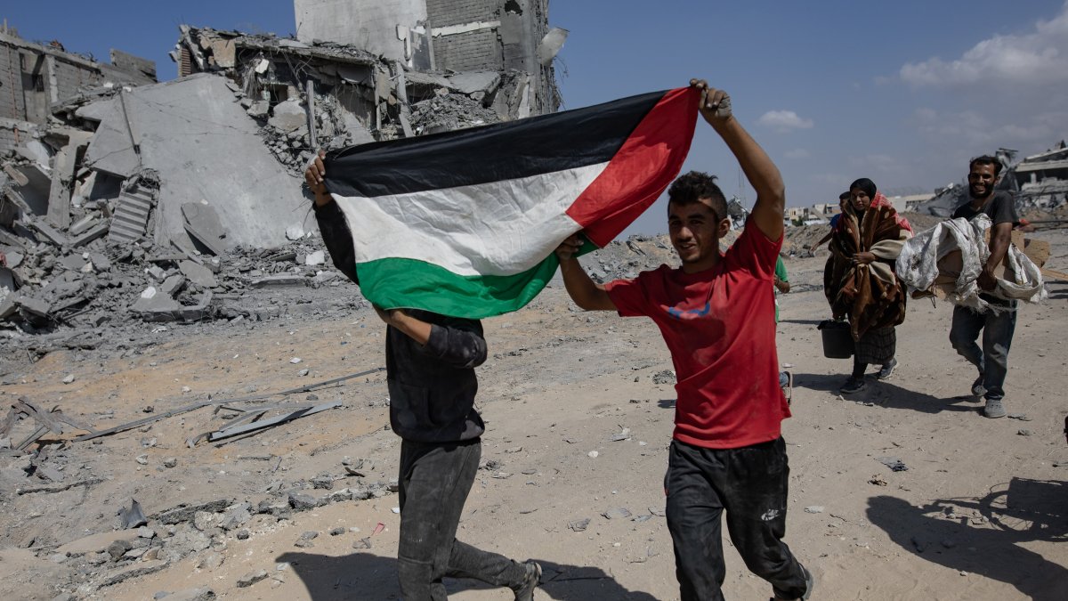 Two children hold the Palestinian flag as they return to inspect their homes after the Israeli army withdrew from some areas east of Khan Yunis in the southern Gaza Strip, Oct. 10, 2025. (EPA Photo)
