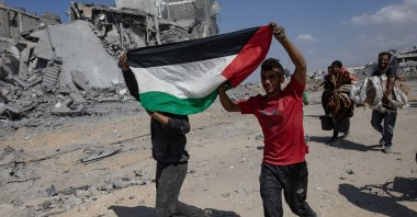 Two children hold the Palestinian flag as they return to inspect their homes after the Israeli army withdrew from some areas east of Khan Yunis in the southern Gaza Strip, Oct. 10, 2025. (EPA Photo)