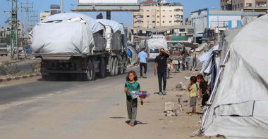 Trucks carrying aid that entered Gaza through the Karm Abu Salem crossing, drive past displacement tents at the Nuseirat refugee camp in the central Gaza Strip, Palestine, Oct. 14, 2025. (AFP Photo)