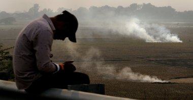 A person checks his mobile phone as farmers burn crop residue after harvest near Bundelkhand expressway, India, Nov. 17, 2024. (AP Photo)