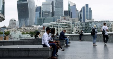 People drink takeaway coffee in view of the City of London skyline in London, U.K., July 25, 2024. (Reuters Photo)