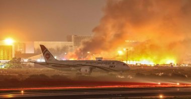 An airline plane stands on the tarmac as firefighters try to extinguish a fire that broke out in the cargo section of Hazrat Shahjalal International Airport in Dhaka, Bangladesh, Oct. 18, 2025. (AFP Photo)