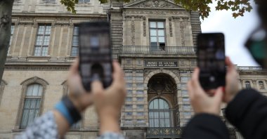 Tourists take photos of the window used by thieves to break into the Louvre Museum in Paris, France, Oct. 20, 2025. (AA Photo)