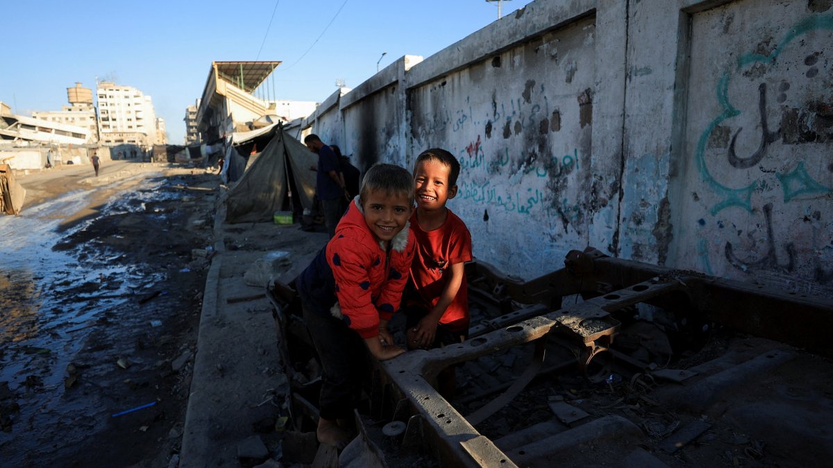 Palestinian children smile as they play on debris next to tents on a street, in Gaza City, Palestine, Oct. 14, 2025. (Reuters Photo)