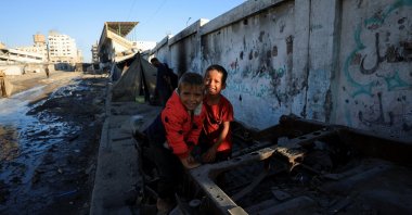 Palestinian children smile as they play on debris next to tents on a street, in Gaza City, Palestine, Oct. 14, 2025. (Reuters Photo)