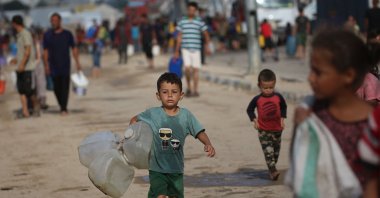 A displaced Palestinian child carries empty jerrycans as people head toward mobile cisterns to get drinking water at the Bureij camp for refugees in the central Gaza Strip, Oct. 6, 2025. (AFP File Photo)
