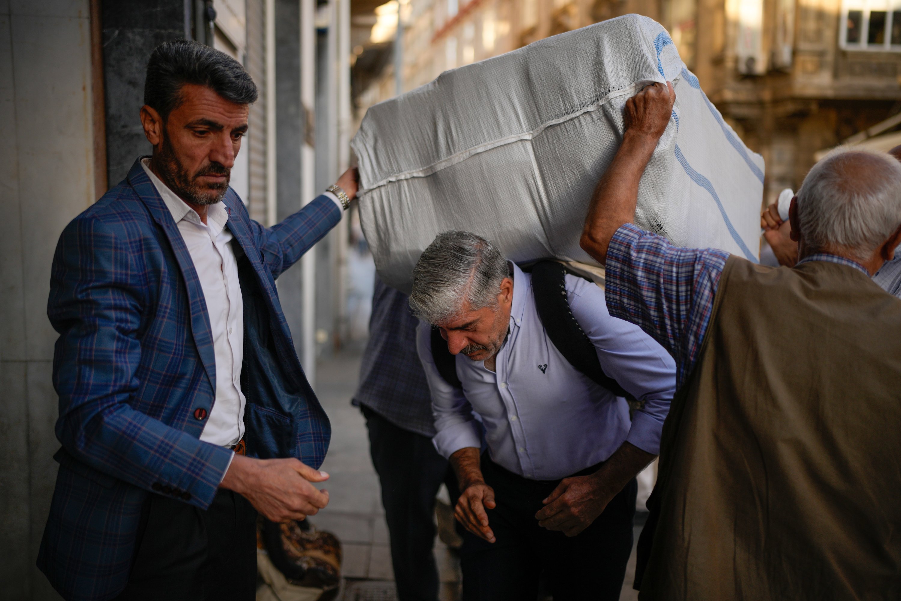 Porters place a load on a coworker's back in the Eminonu commercial area, Istanbul, Türkiye, Sept. 24, 2025. (AP Photo)