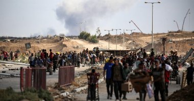 A plume of smoke rises in the background as Palestinians return from a food distribution point run by the U.S. and Israeli-backed Gaza Humanitarian Foundation (GHF) group, Gaza Strip, Palestine, Oct. 5, 2025. (AFP Photo)