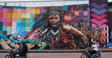 Motorcyclists ride past a mural depicting a powerful woman on a street wall in Conakry, Guinea, Oct. 19, 2025. (AP Photo)