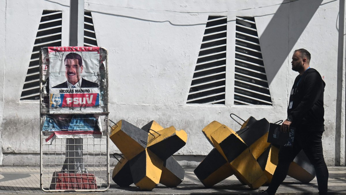 A man walks past a poster of Venezuelan President Nicolas Maduro and an anti-tank barricade in Caracas, Oct. 28, 2025. (AFP Photo)