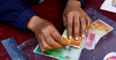 Palestinian woman Manal al-Saidi repairs damaged banknotes on the side of a street, amid a cash crisis, in Nuseirat, Gaza Strip, Palestine, Oct. 27, 2025. (Reuters Photo)