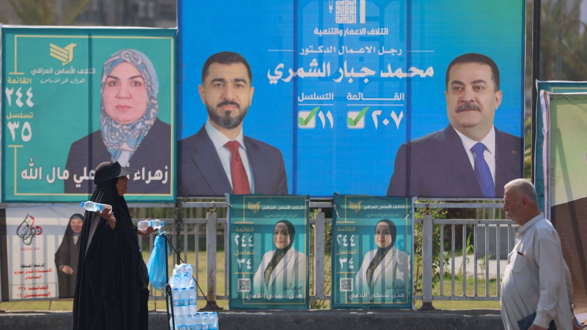 A woman walks past electoral billboards, including one bearing a portrait of Prime Minister Mohammed Shia Al Sudani (R), as she sells water, central Baghdad, Iraq, Oct. 19, 2025. (AFP Photo)