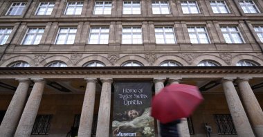 A man with an umbrella walks past a banner with the title &quot;Home of Taylor Swift&#039;s Ophelia&quot; outside a museum, Wiesbaden, Germany, Nov. 2, 2025. (AFP Photo)