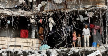A Palestinian man and children stand at a heavily damaged building surrounded by rebar and rubble, in Gaza, Palestine, Nov. 2, 2025. (Reuters Photo)