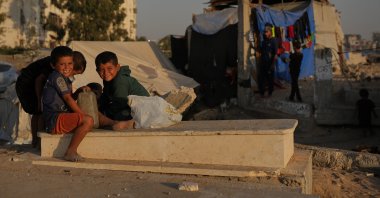 Palestinian children sit on a grave near makeshift tents for displaced people that were set up in a cemetery in Khan Younis, in the southern Gaza Strip, Palestine, Oct. 31, 2025. (AP Photo)
