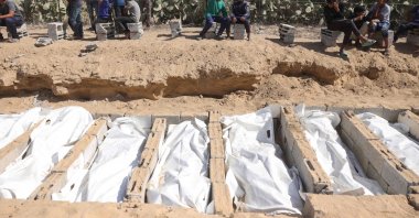 Children watch as the remains of unidentified Palestinians are being buried at a cemetery in Deir al-Balah, in the central Gaza Strip, after they were returned by Israel under a U.S.-brokered cease-fire deal, Oct. 22, 2025. (AFP Photo)