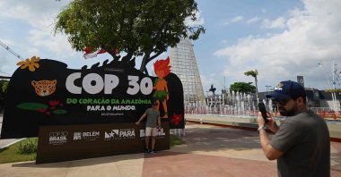 A tourist poses for a picture with a banner of COP30 depicting its mascot, Curupira, Belem, Para State, Brazil, Nov. 9, 2025. (AFP Photo)