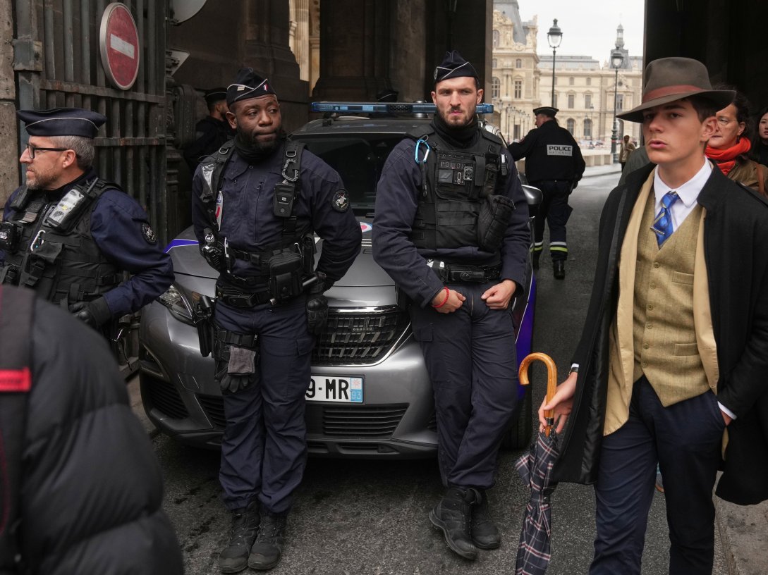 Pedro Elias Garzon Delvaux (R) walks past as police officers block an entrance to the Louvre after thieves carried out a daylight raid on French crown jewels, Paris, France, Oct. 19, 2025. (AP Photo)