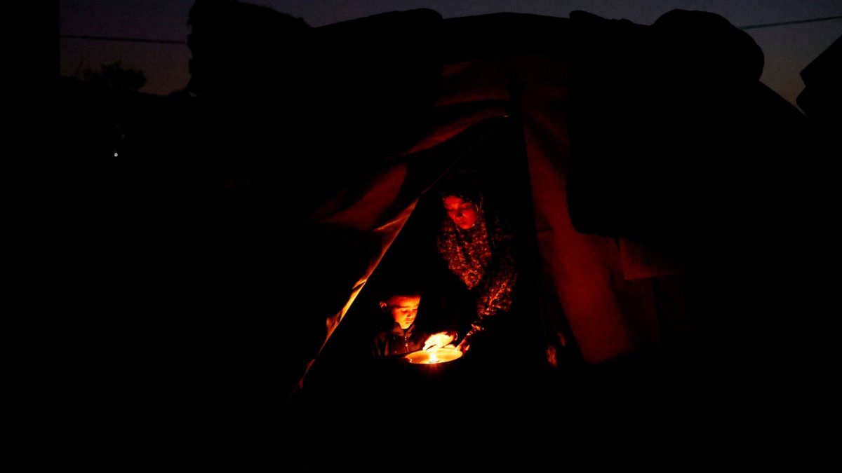 Displaced Palestinian Hanan al-Joujou sits with her child at the entrance of their tent, during a power cut, in Nuseirat, central Gaza Strip, Oct. 31, 2025. (Reuters Photo)