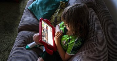 Six-year-old Enrique Navarro sits on a couch with his iPad watching a show on YouTube at his home in western Sydney, Australia, Oct. 30, 2025. (AFP Photo)