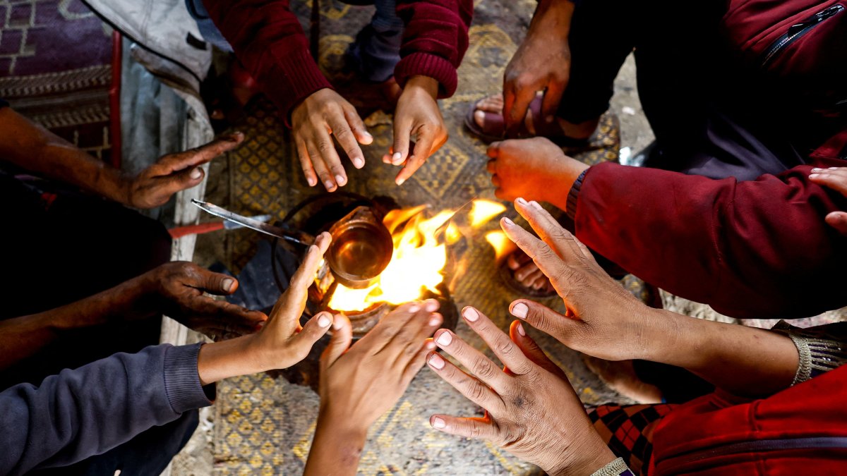 Displaced Palestinians warm their hands inside a tent, on a rainy day in the central Gaza Strip, November 16, 2025. REUTERS/Mahmoud Issa