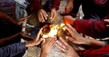Displaced Palestinians warm their hands inside a tent, on a rainy day in the central Gaza Strip, November 16, 2025. REUTERS/Mahmoud Issa