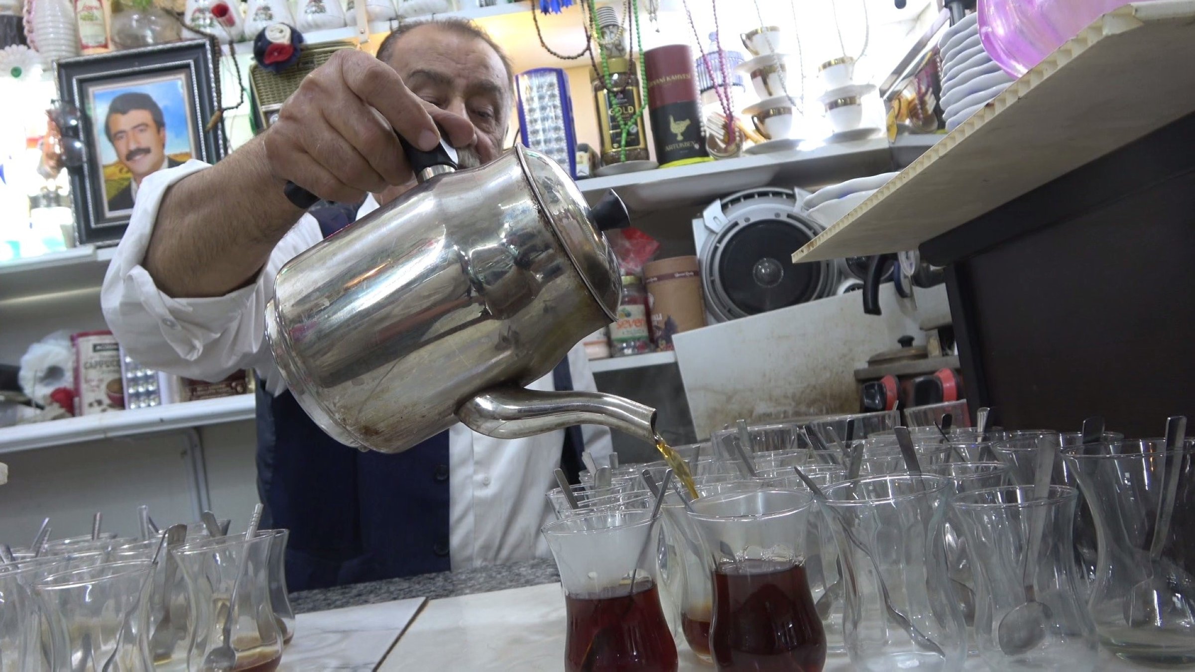 Celal Çazım carefully pours tea into traditional glasses at his tea house, welcoming visitors in Cizre, Türkiye, Nov. 17, 2025. (IHA Photo)