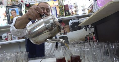Celal Çazım carefully pours tea into traditional glasses at his tea house, welcoming visitors in Cizre, Türkiye, Nov. 17, 2025. (IHA Photo)