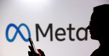 A teenager poses for a photo while holding a smartphone in front of a Meta logo in this illustration taken Sept. 11, 2025. (Reuters File Photo)