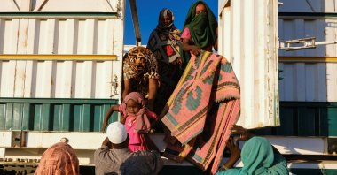 A displaced woman from el-Fasher hands a child to a volunteer to help them get down from a truck, at a displacement camp in Al-Dabba, Sudan, Nov. 19, 2025. (Reuters Photo)