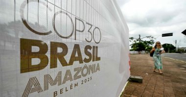 A woman walks past a banner with the COP30 UN Climate Change Conference logo outside the Hangar Convention and Exhibition Center, Belem, Brazil, Nov. 5, 2025. (AFP Photo)