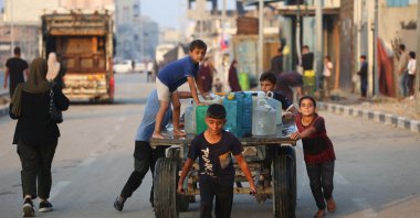 A boy pulls a donkey cart laden with containers carrying potable water, as other displaced Palestinian children help push it along a road in the Bureij refugee camp, in the central Gaza Strip, Nov. 10, 2025. (AFP File Photo)