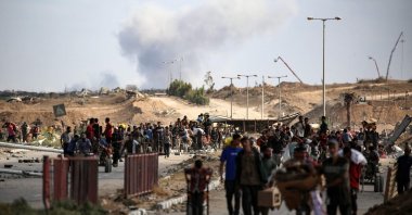 A plume of smoke rises in the background as Palestinians return from a food distribution point run by the U.S. and Israeli-backed Gaza Humanitarian Foundation (GHF) group, Gaza Strip, Palestine, Oct. 5, 2025. (AFP File Photo)