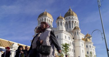 Two women walk past people waiting in line to visit the National Cathedral, Bucharest, Romania, Oct. 30, 2025. (Reuters Photo)