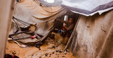 A Palestinian child sits in a tent as rain water runs past, at a makeshift camp housing displaced Palestinians in Deir al-Balah, central Gaza Strip, Palestine, Nov. 25, 2025. (AFP Photo)