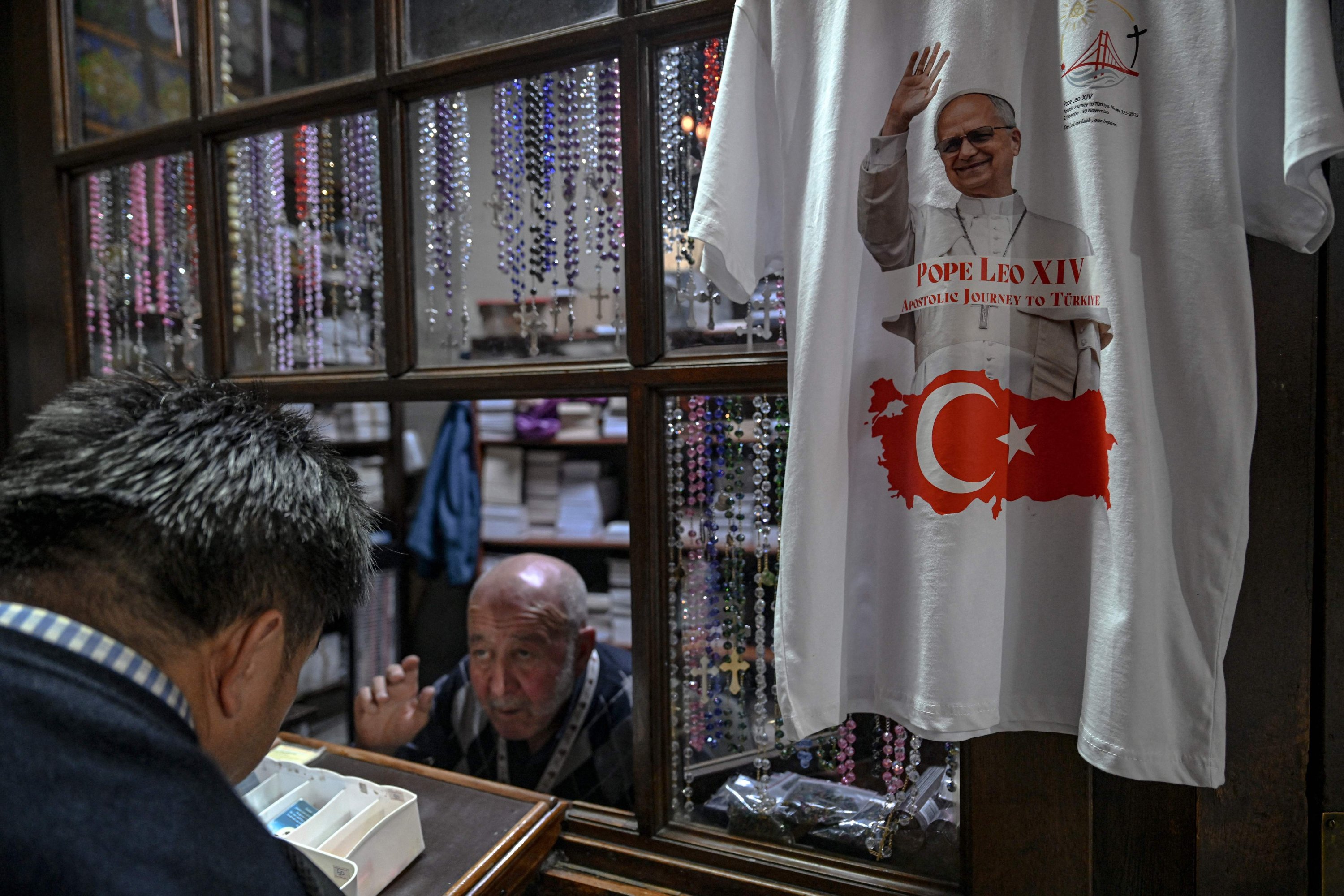An employee of Saint Anthony of Padua Church sells candles and religious books as a t-shirt bearing a portrait of Pope Leo XIV and a Turkish flag, Istanbul, Türkiye, Nov. 24, 2025. (AFP Photo)