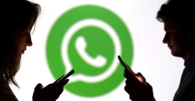 Teenagers pose for a photo while holding smartphones in front of a WhatsApp logo in this illustration taken Sept. 11, 2025. (Reuters Photo)
